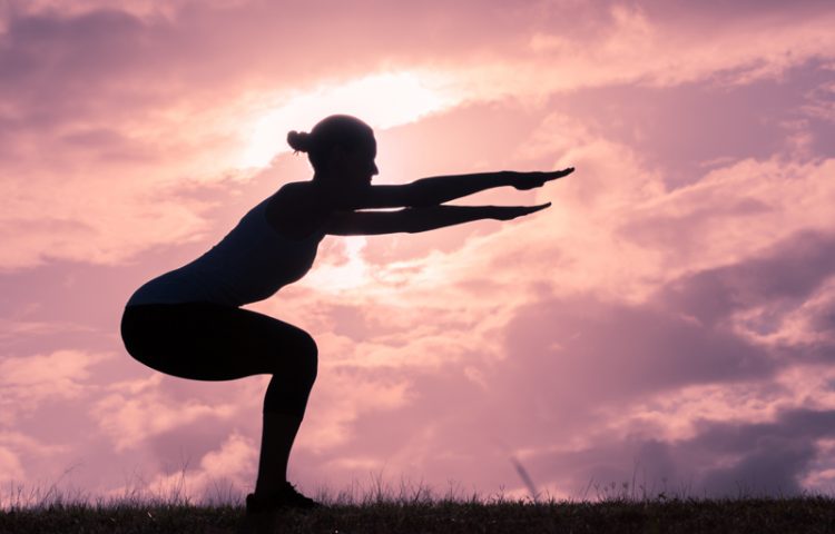 Woman doing squats while the sun rises