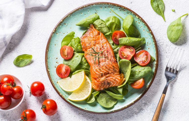 Baked salmon fish fillet with fresh salad from spinach and tomatoes. Top view on white background.